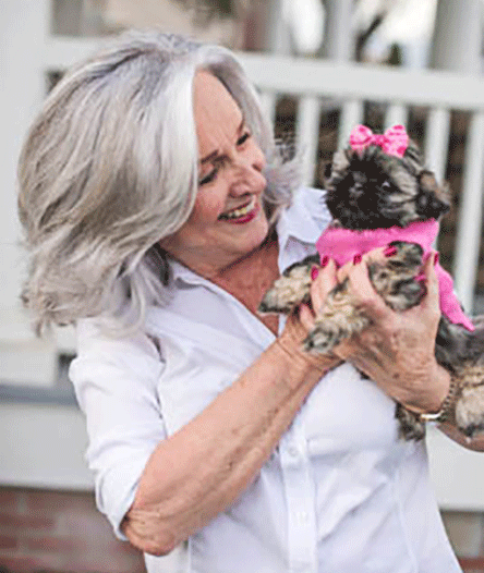 Joan smiling holding a cute little dog in a pink outfit